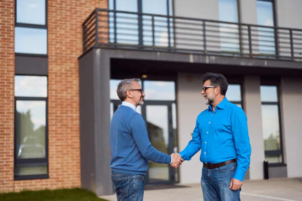 Two men shaking hands outside a modern building, symbolizing professional junk removal and property management services.