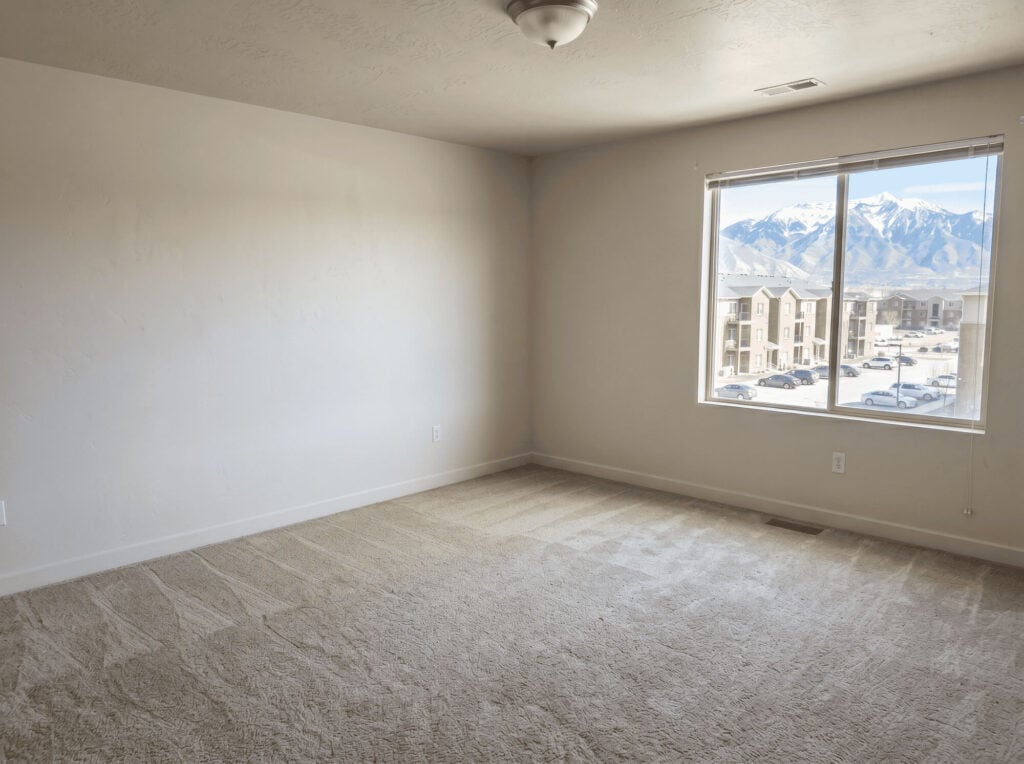 Empty living room with large window showing mountain view and neighboring buildings.
