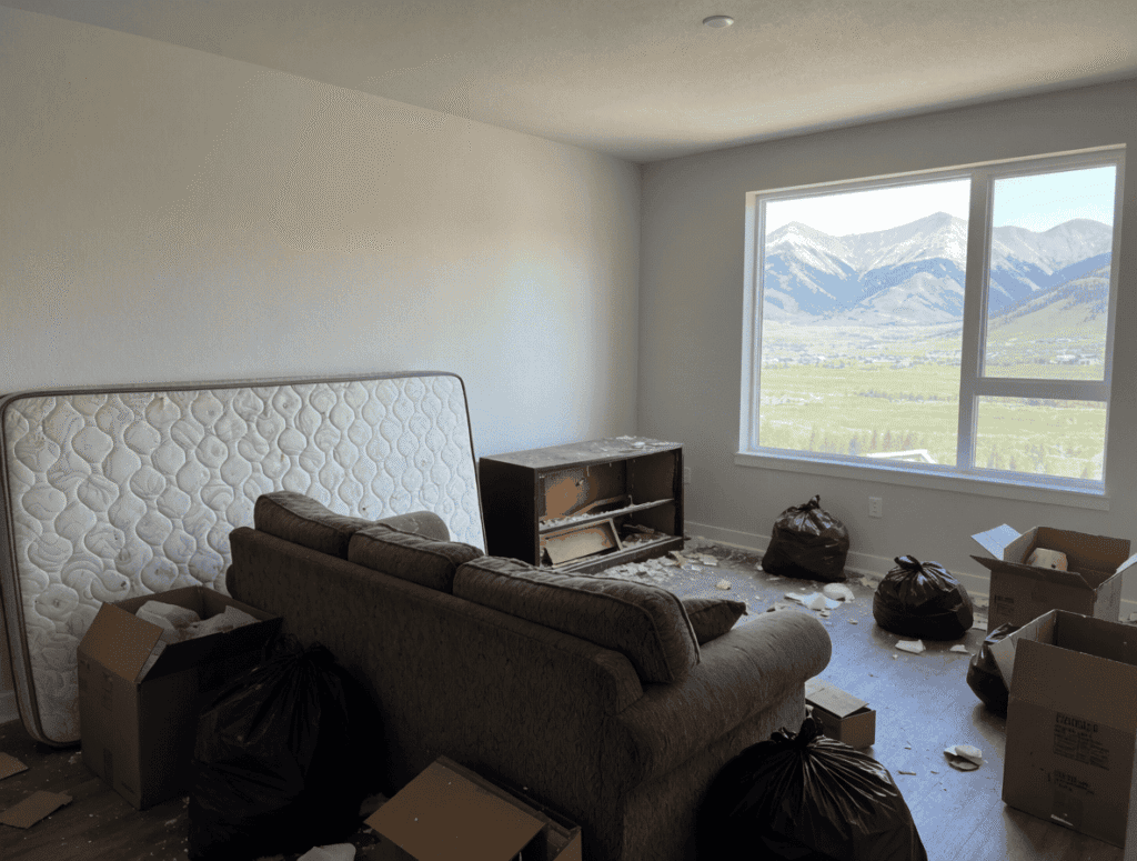 Interior of a cluttered living room with trash bags, boxes, and a mattress, ready for junk removal services.