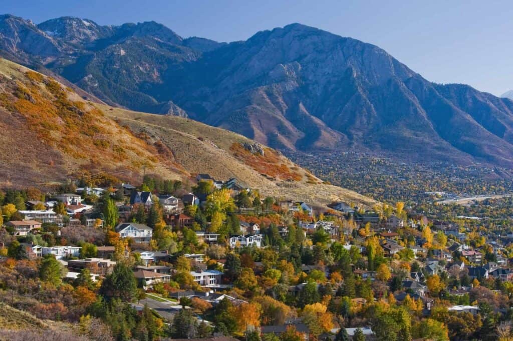 A scenic mountain landscape overlooking a suburban area with colorful fall foliage.