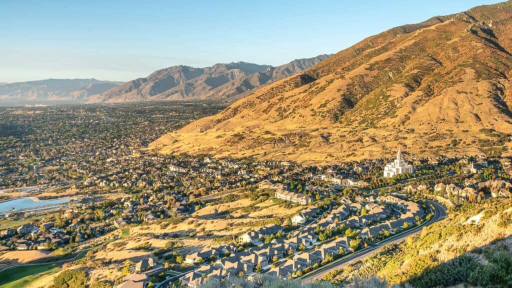 Aerial view of a mountain range overlooking a city with residential neighborhoods and winding roads during golden hour.