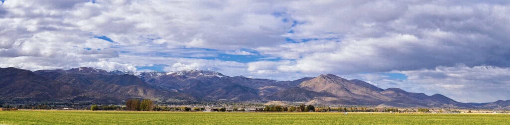 Mountain landscape with blue sky and clouds over green fields and distant mountains.