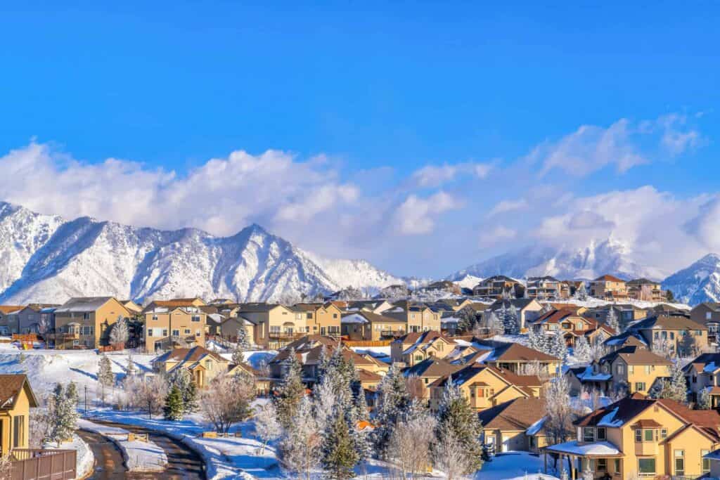 Snow-covered houses and trees in a mountain suburb during winter daytime.